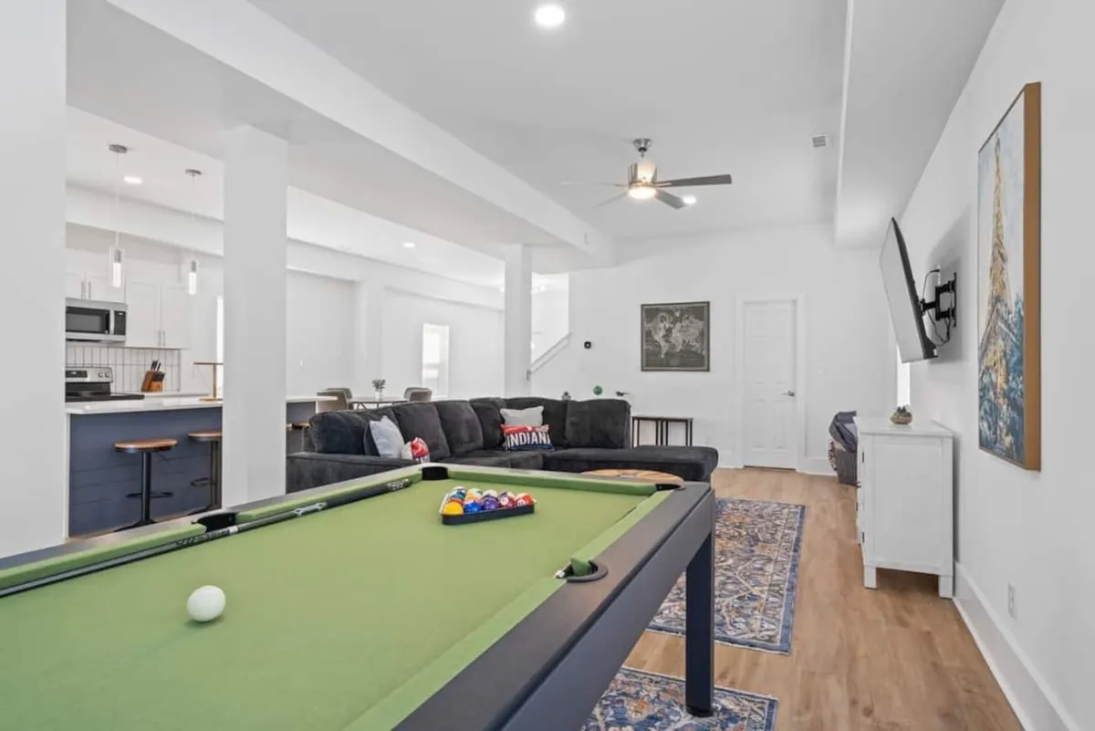 The hero image captures a stylish, spacious living area centered around a modern pool table, with a comfortable sofa and television inviting guests to relax, socialize, and enjoy game nights together. The room exudes a casual, welcoming vibe, perfect for gatherings and family fun.