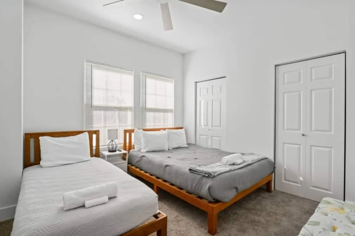 A well-lit bedroom featuring two cozy beds, a central nightstand, and sun streaming in through large windows—ideal for families or groups sharing a restful night together.