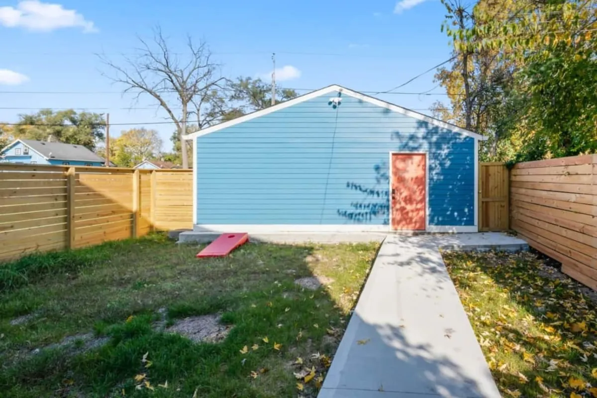 This image shows the inviting blue exterior wall of the home with a welcoming red door and a clear pathway leading up to it. The scene is set during the golden hour, suggesting a vibrant yet cozy atmosphere perfect for group arrivals or evening returns after exploring the city.